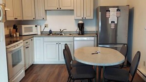 Une cuisine compacte avec des meubles blancs, un four à micro-ondes, une machine à café, un réfrigérateur et une petite table à manger avec quatre chaises.