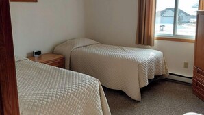 Une chambre avec deux lits, une table de chevet et une fenêtre donnant sur un bâtiment.