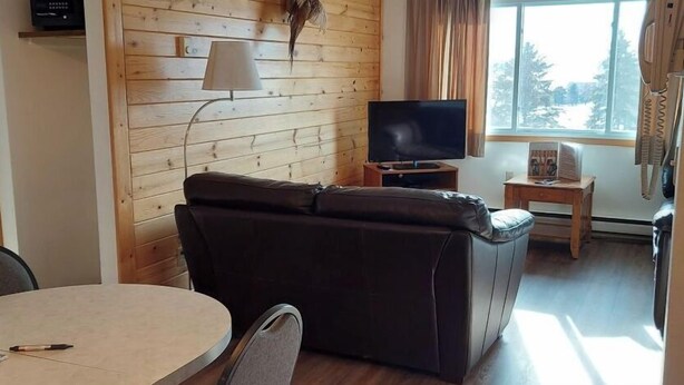 Une pièce confortable avec un canapé en cuir, un téléviseur posé sur un meuble en bois, une petite table et une fenêtre avec des rideaux.