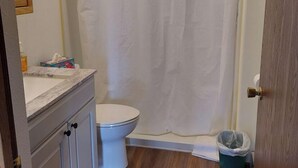 Une salle de bain avec des toilettes blanches, un rideau de douche, une poubelle et un comptoir en marbre.
