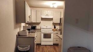 A compact kitchen with white cabinets, a microwave, an oven, and a trash bin. - Deluxe 2 Bedrooms 8 XL Twin Beds, 2 Bathrooms Ground Floor #7 (Devils Lake)