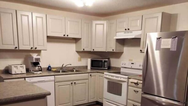 A kitchen with white cabinets, a stainless steel refrigerator, a microwave, a stove, and a toaster. - Deluxe 2 Bedrooms 8 XL Twin Beds, 2 Bathrooms Ground Floor #7 (Devils Lake)