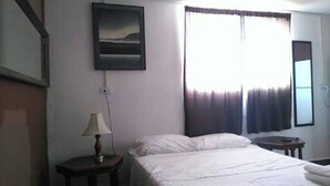 A hotel room with a bed, a nightstand, a lamp, a painting, and a window with curtains.