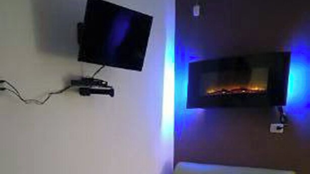 A room with a flat-screen TV mounted on the wall, a green sofa, and two green armchairs.