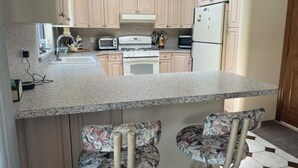A kitchen with a granite countertop, a stove, a refrigerator, and two bar stools with floral upholstery. - Spacious Vacation 4BR Home Near Southold Beach, Greenport, and Top Wineries (Southold)