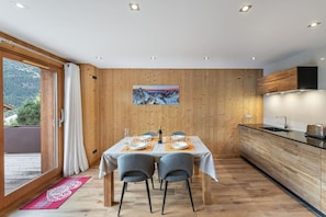 Una cucina moderna con pannelli in legno, un'area pranzo con due sedie, un tavolo imbandito per due e vista sull'esterno tramite una porta scorrevole.