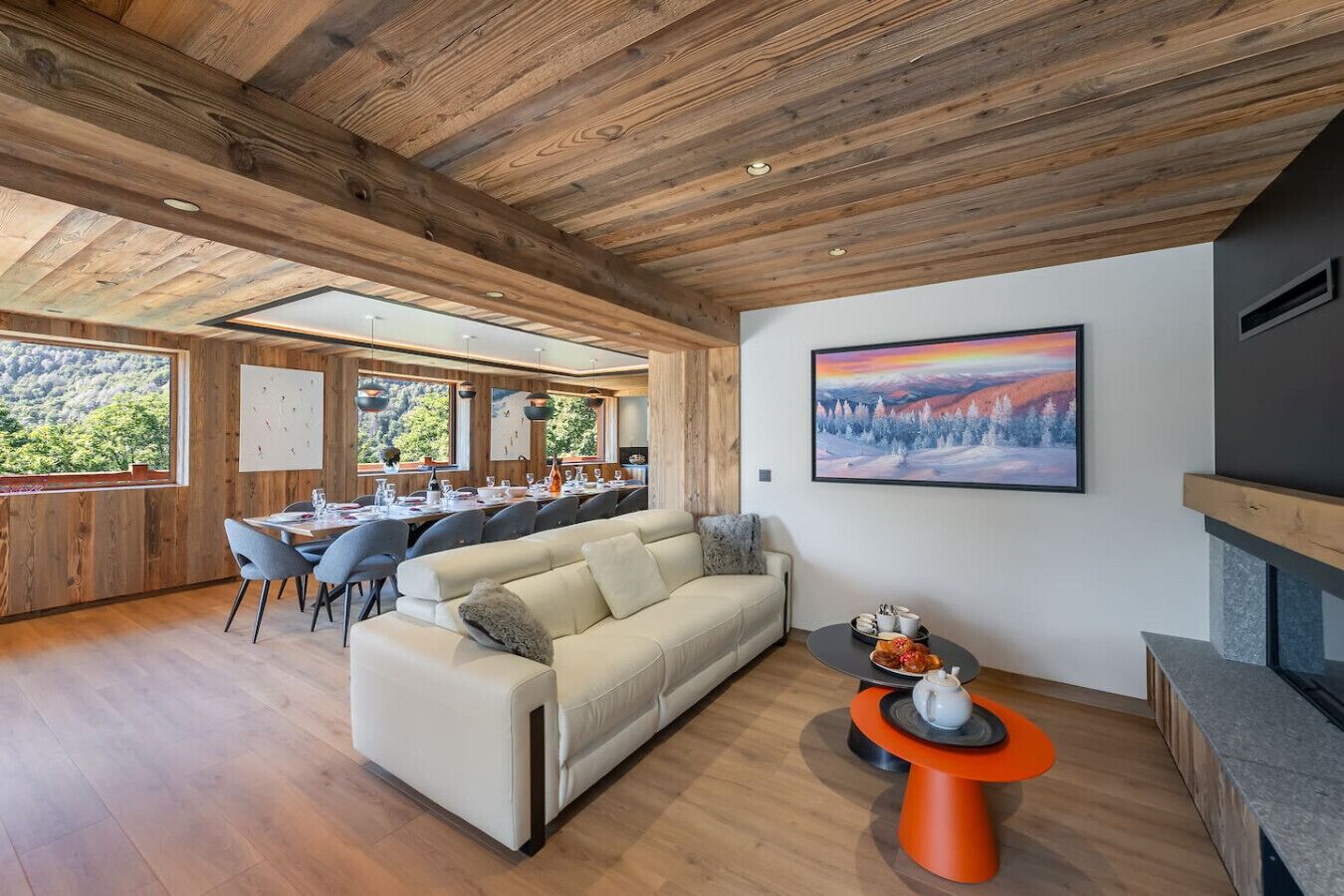 Un vaste espace de vie doté d’un plafond en bois, d’un canapé, d’une table à manger pouvant accueillir six personnes et d’une cheminée.