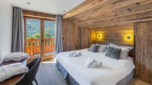 Un dormitorio con techo de madera, cama con almohadas, mesa con toallas y un balcón con vistas a zonas verdes.