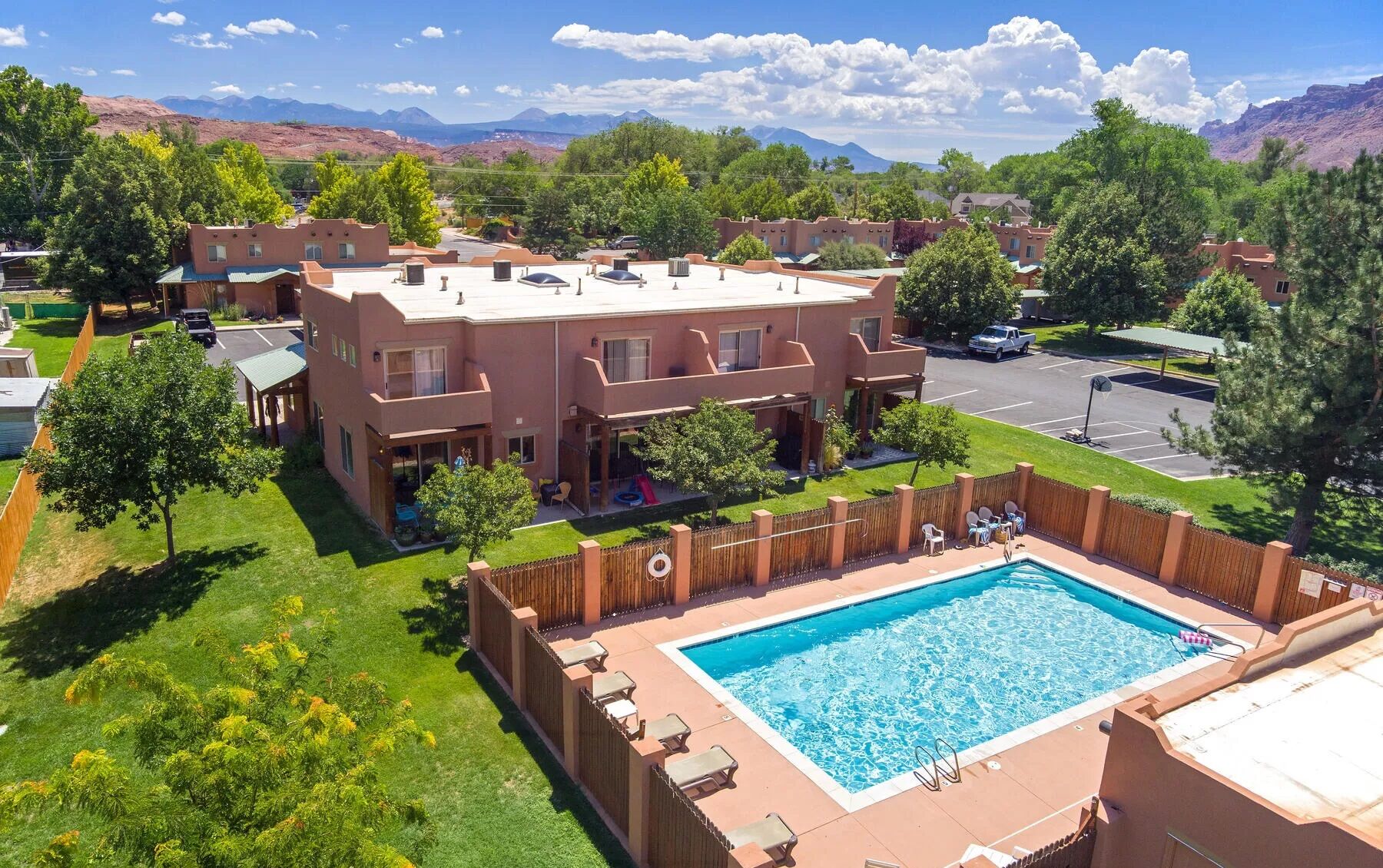 A residential building with a swimming pool, surrounded by greenery and mountains in the background.