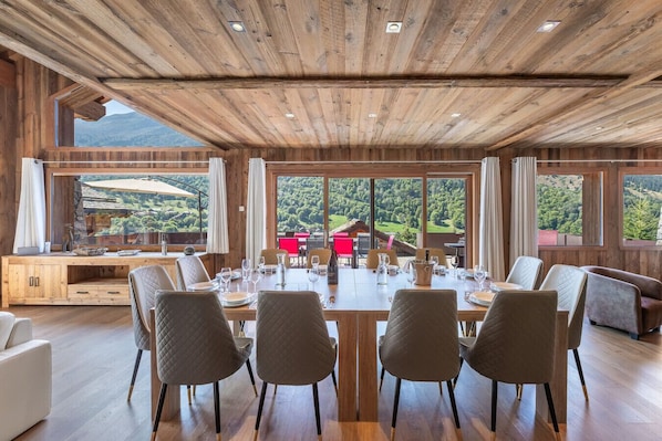 Un espace repas doté d’un plafond en bois, de grandes fenêtres et d’une vue sur les montagnes.