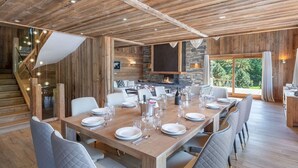 Un comedor espacioso con una larga mesa de madera dispuesta para una comida, una chimenea y vistas al exterior.