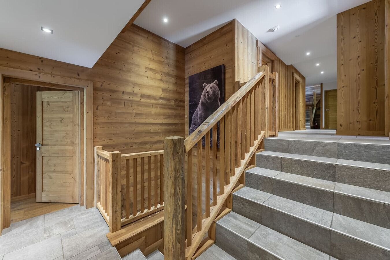 Eine Holztreppe mit einem Bärenbild, einer Holztür und einem Fliesenboden.