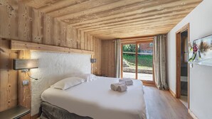 Habitación con paneles de madera, una cama, una mesita de noche, una lámpara de pared y un ventanal con cortinas.