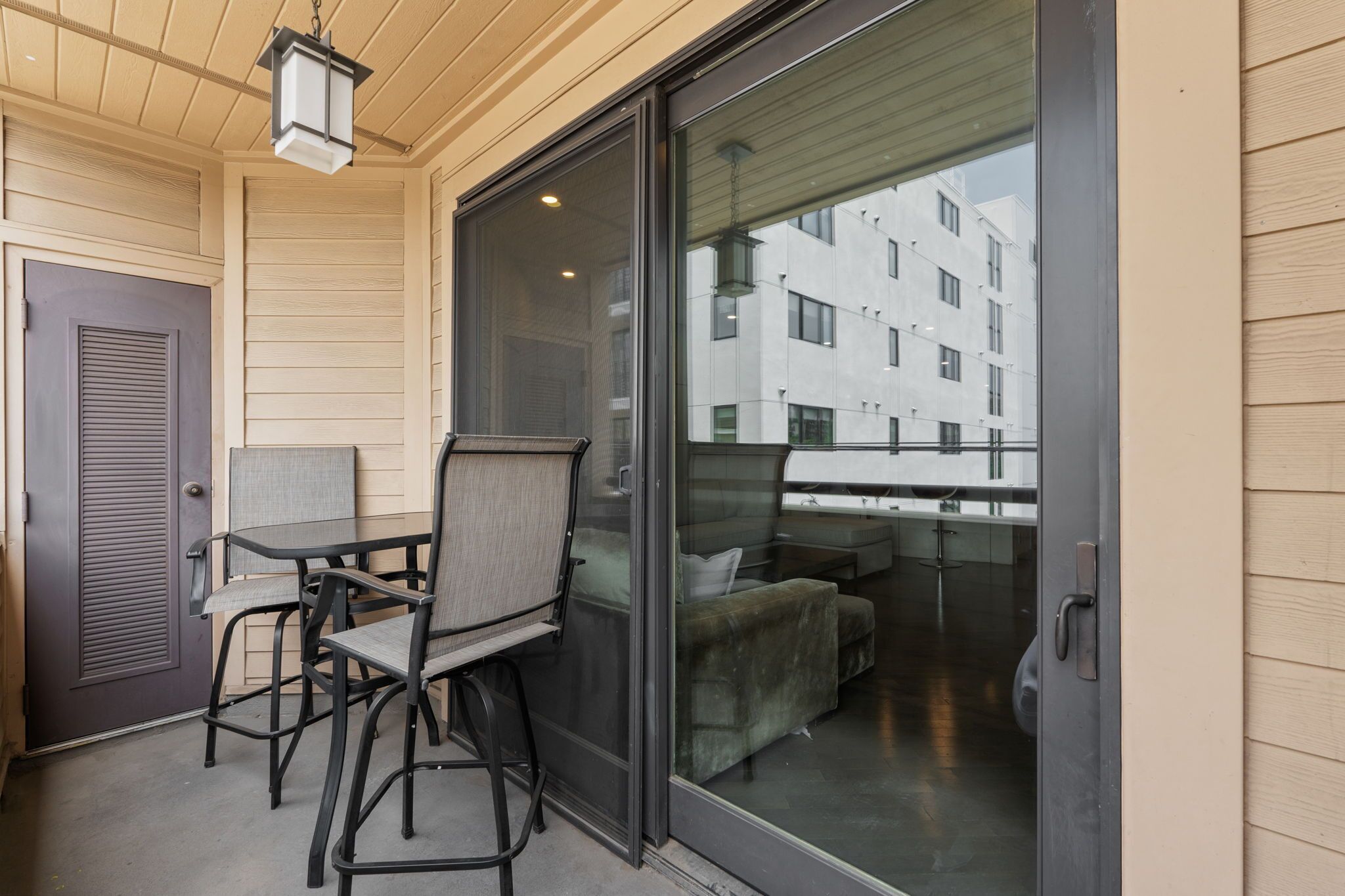 Un balcon avec une table et des chaises, une porte-fenêtre coulissante et une vue sur un immeuble.