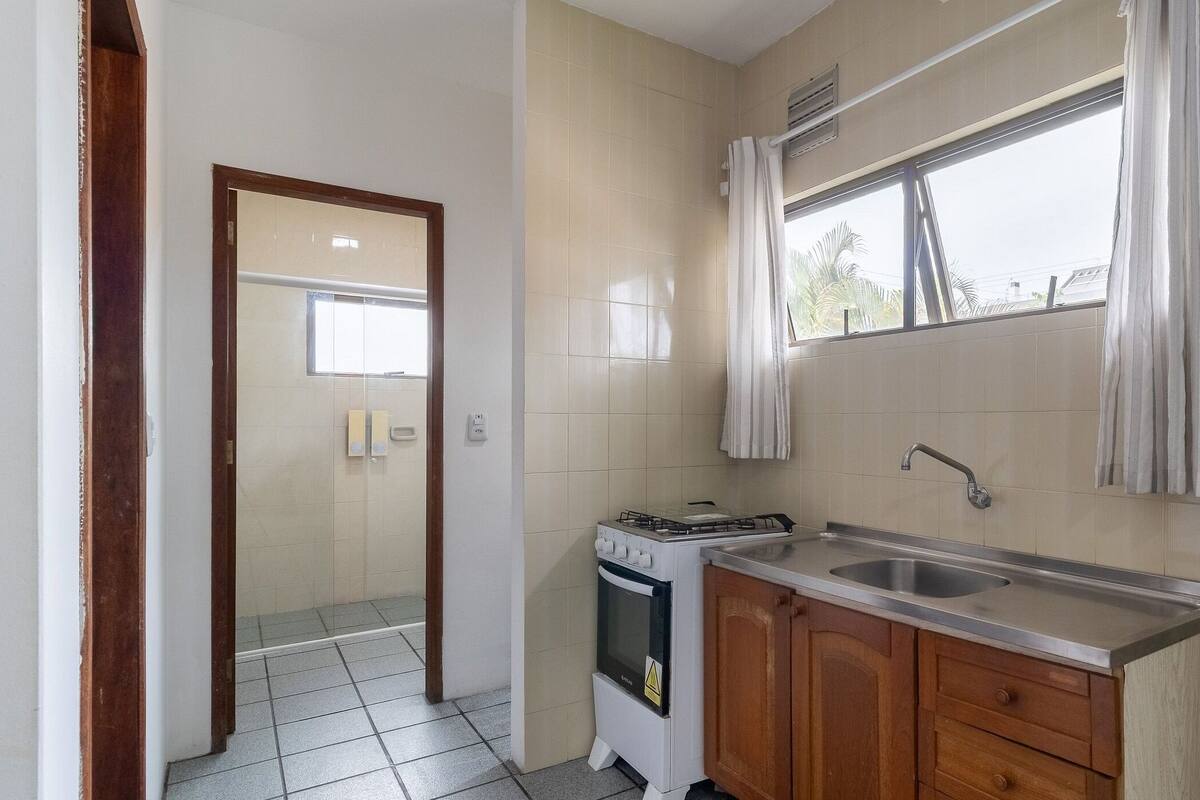 A compact kitchen with a gas stove, a sink, wooden cabinets, and a window with curtains.