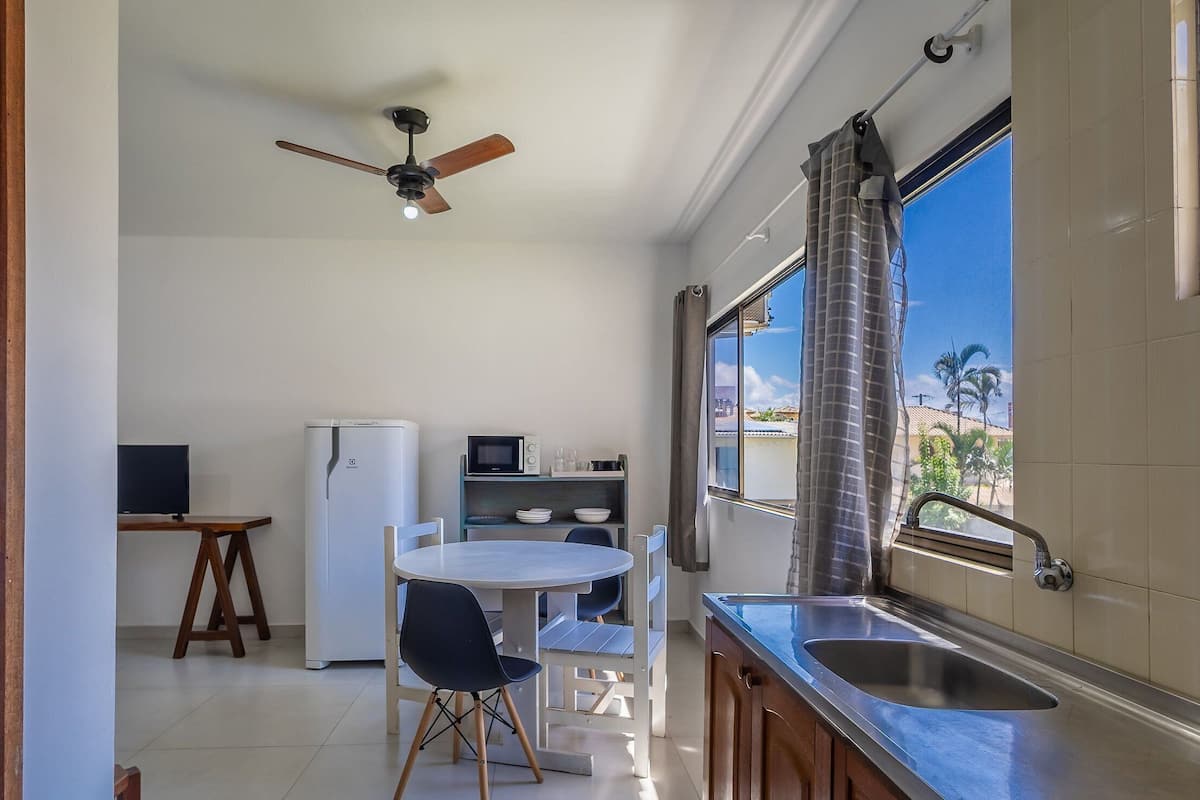 A compact kitchen with a dining area, a ceiling fan, and a view of palm trees through the window.