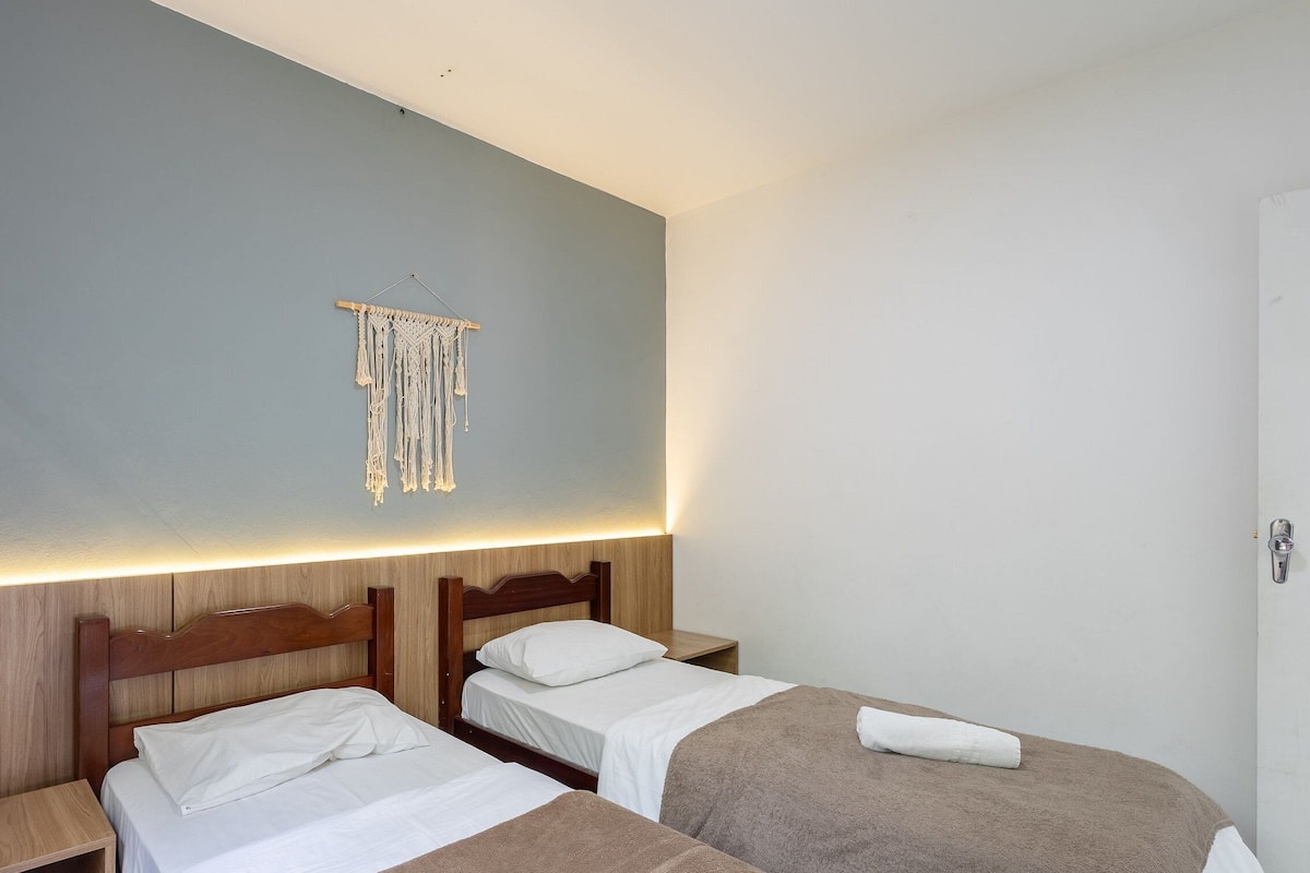 A hotel room with two wooden beds, a macrame wall hanging, and a bedside table with a lamp.