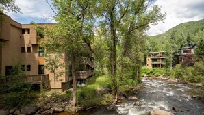 Un hotel lungo il fiume, composto da diversi edifici, con una terrazza in legno e un ruscello roccioso.