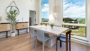 A modern dining area with a large window, a wooden table, and several chairs. - Luxury 4BR Condo | Pool, Hot Tub & Mtn Views! (Snowmass Village)