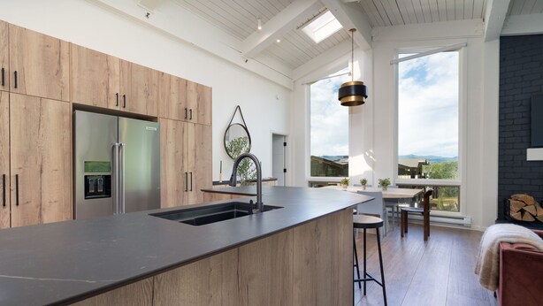 A modern kitchen with wooden cabinets, a stainless steel refrigerator, and a large island with a sink. - Luxury 4BR Condo | Pool, Hot Tub & Mtn Views! (Snowmass Village)