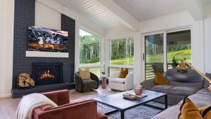 A modern living room with a fireplace, comfortable seating, and large windows offering a view of the outdoors. - Luxury 4BR Condo | Pool, Hot Tub & Mtn Views! (Snowmass Village)