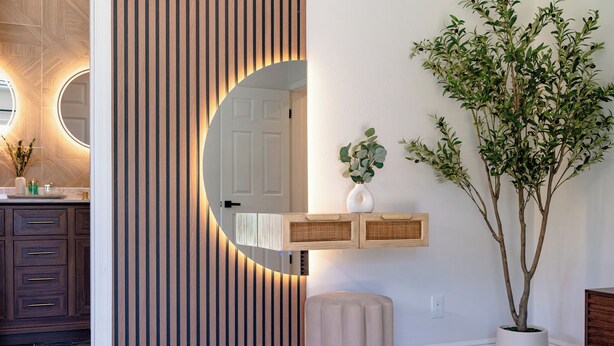 A modern bathroom with a wooden vanity, a round mirror, and a potted plant.