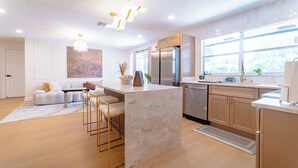 A modern kitchen with a marble island, stainless steel appliances, and a large window providing natural light.