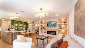 A modern living room with a fireplace, a dining area, and a kitchen with wooden cabinets.