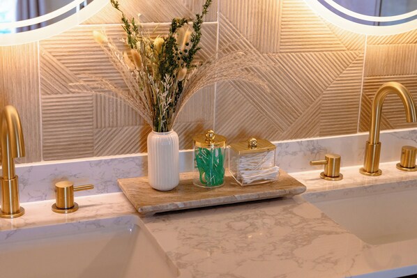 A bathroom with a marble sink, gold faucets, and a decorative arrangement including a vase with dried plants.