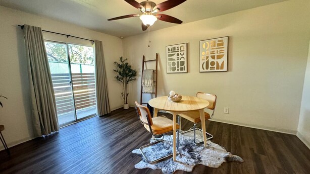 A dining area with a round table, two chairs, a ceiling fan, and artwork on the wall.