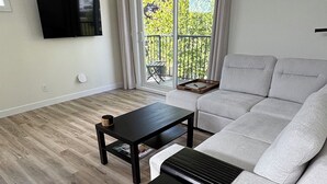 Een moderne woonkamer met een grijze bank, twee zwarte salontafels en een flatscreen televisie aan de muur.