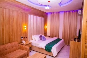 Quarto de hotel com uma cama, um sofá, uma mesa de cabeceira com abajur e cortinas.