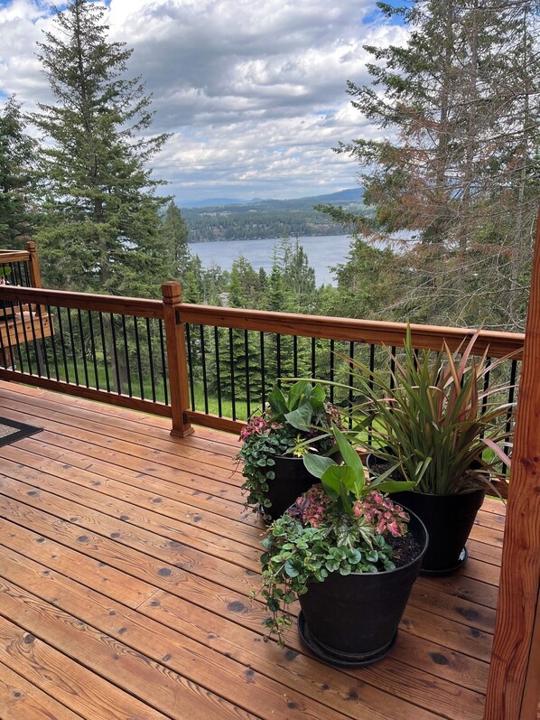 A wooden deck with a railing, potted plants, and a view of a lake and mountains. - B&B with fireplace, 4 TV's, deck, billiards, firepit & great view of Hayden Lake (Coeur d'Alene)