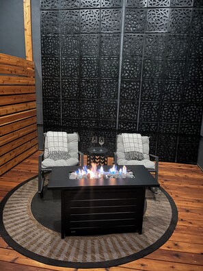 A cozy seating area with two chairs, a central table with a fire feature, and a decorative wall panel. - B&B with fireplace, 4 TV's, deck, billiards, firepit & great view of Hayden Lake (Coeur d'Alene)