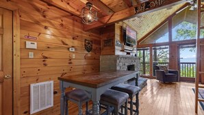 A wooden cabin interior with a bar area, a fireplace, and a large window overlooking a scenic view. - The Good Place: Cabin with Mountain View (Sevierville)
