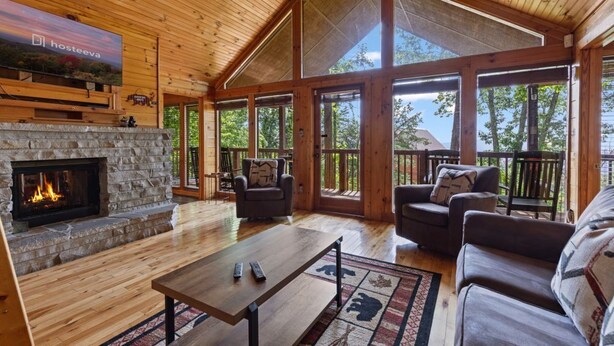 A spacious room with a stone fireplace, wooden ceiling, large windows, and a cozy seating area. - The Good Place: Cabin with Mountain View (Sevierville)