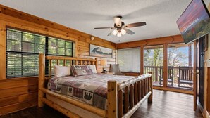 A wooden cabin bedroom with a bed, a ceiling fan, and a TV. - The Good Place: Cabin with Mountain View (Sevierville)