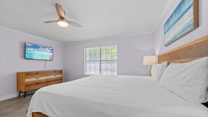 Una habitación de hotel con una cama, un aparador de madera, un televisor, una ventana y un ventilador de techo.