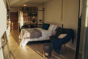 A modern bedroom with a bed, a chair, a small stool, and a desk with a chair.