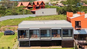 A modern house with a large glass balcony, a swimming pool, and a car parked nearby. - Pousada Austral Suítes (Imbituba)