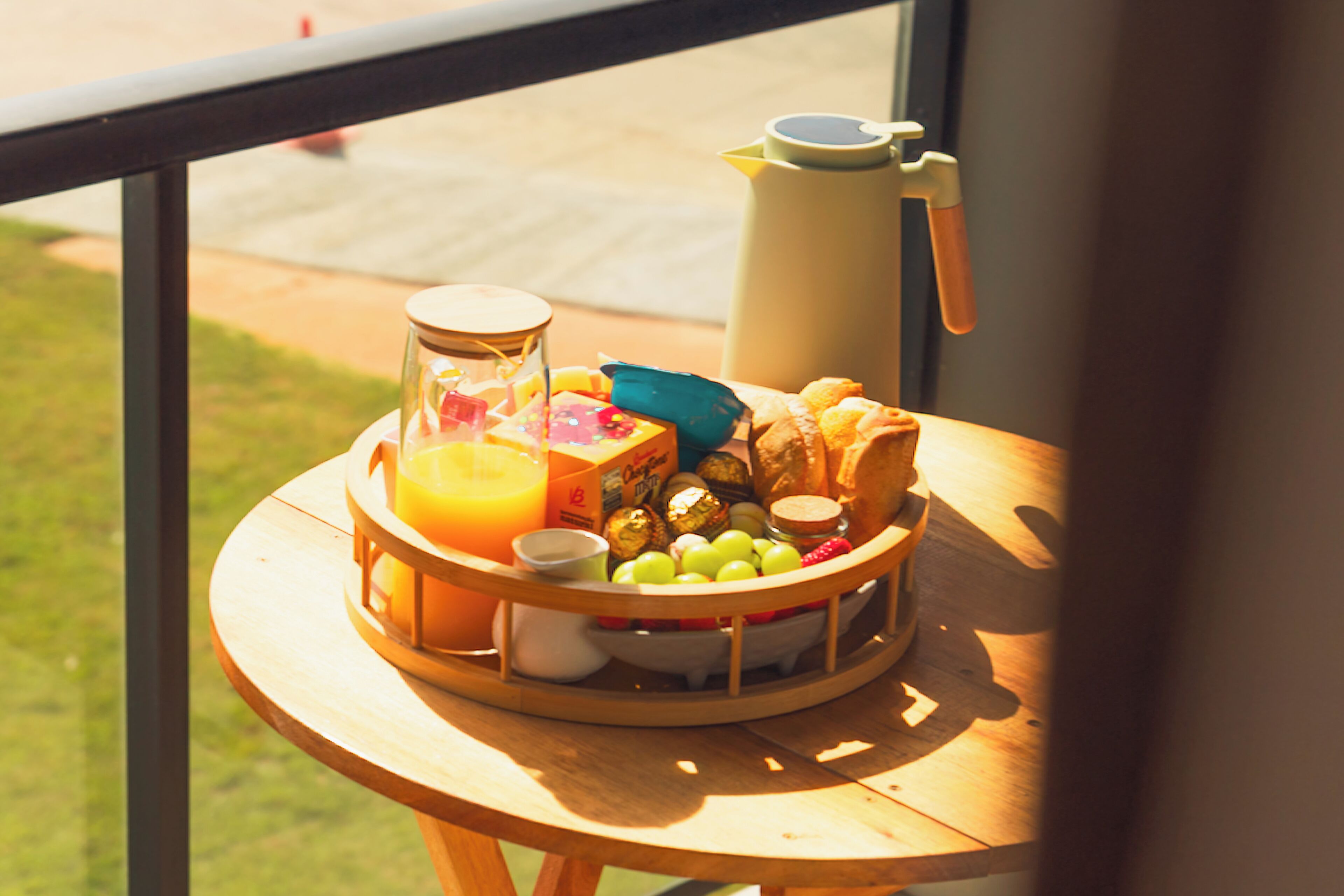 Una bandeja de desayuno con diversos alimentos y una cafetera sobre una mesa junto a una ventana.