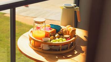 Una bandeja de desayuno con diversos alimentos y una cafetera sobre una mesa junto a una ventana.