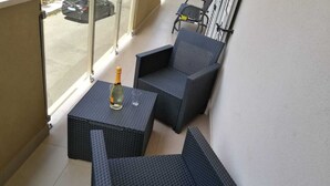 Un balcon avec deux fauteuils en osier et une petite table, une bouteille de champagne et une vue sur la rue.