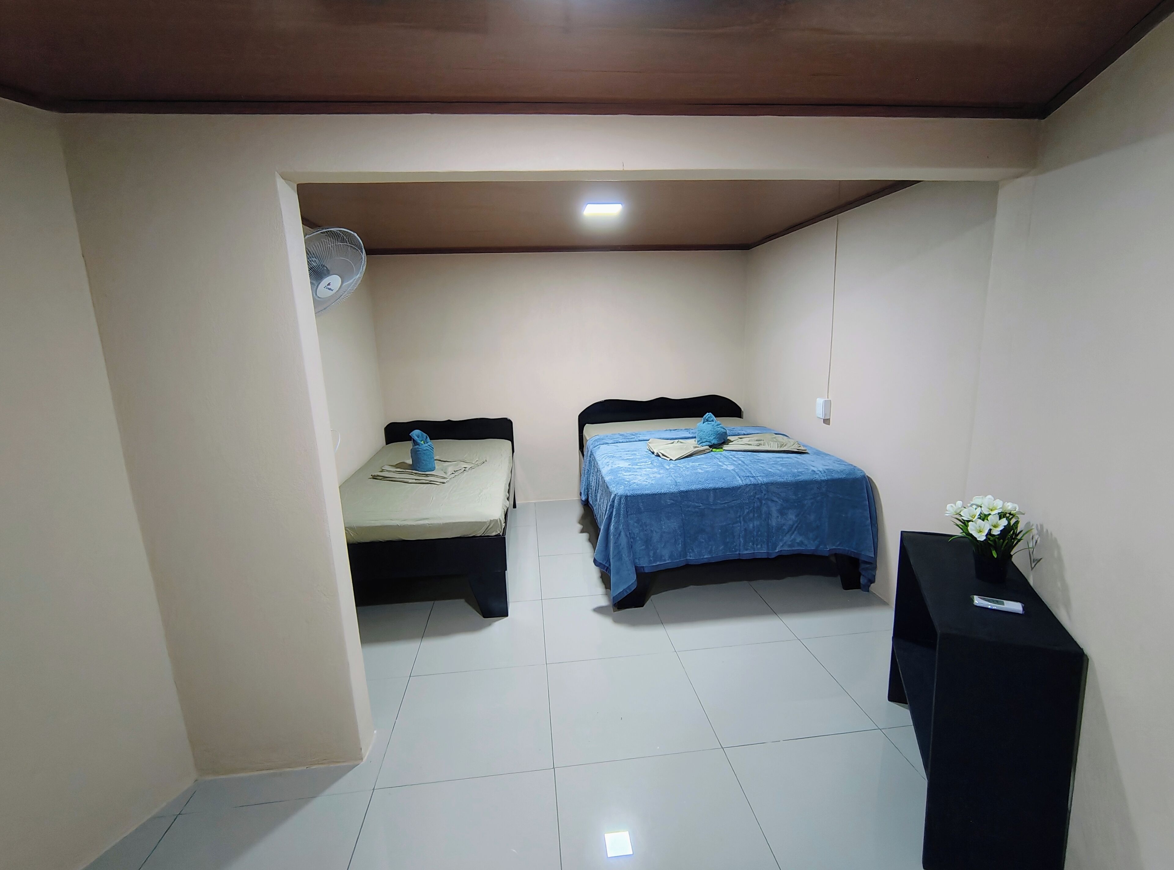 Een nette, kleine kamer met twee bedden, een ventilator en een klein tafeltje met een bloemenvaas.