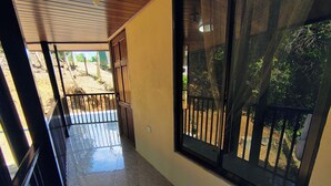 Um corredor com piso de azulejos, uma porta de madeira e uma janela grande com vista para um jardim.