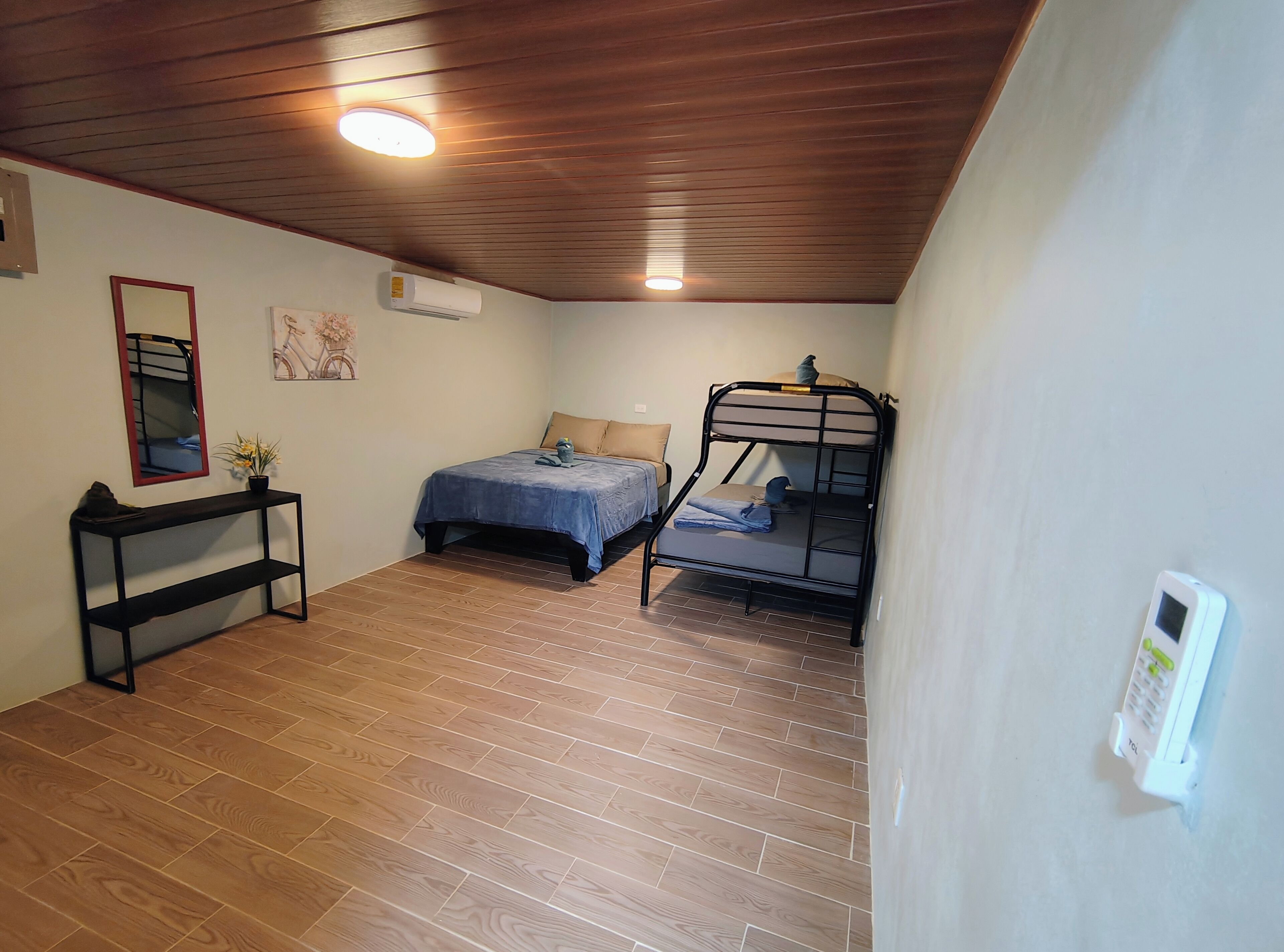 A room with a bunk bed, a bedside table, a mirror, and a wall-mounted air conditioner.