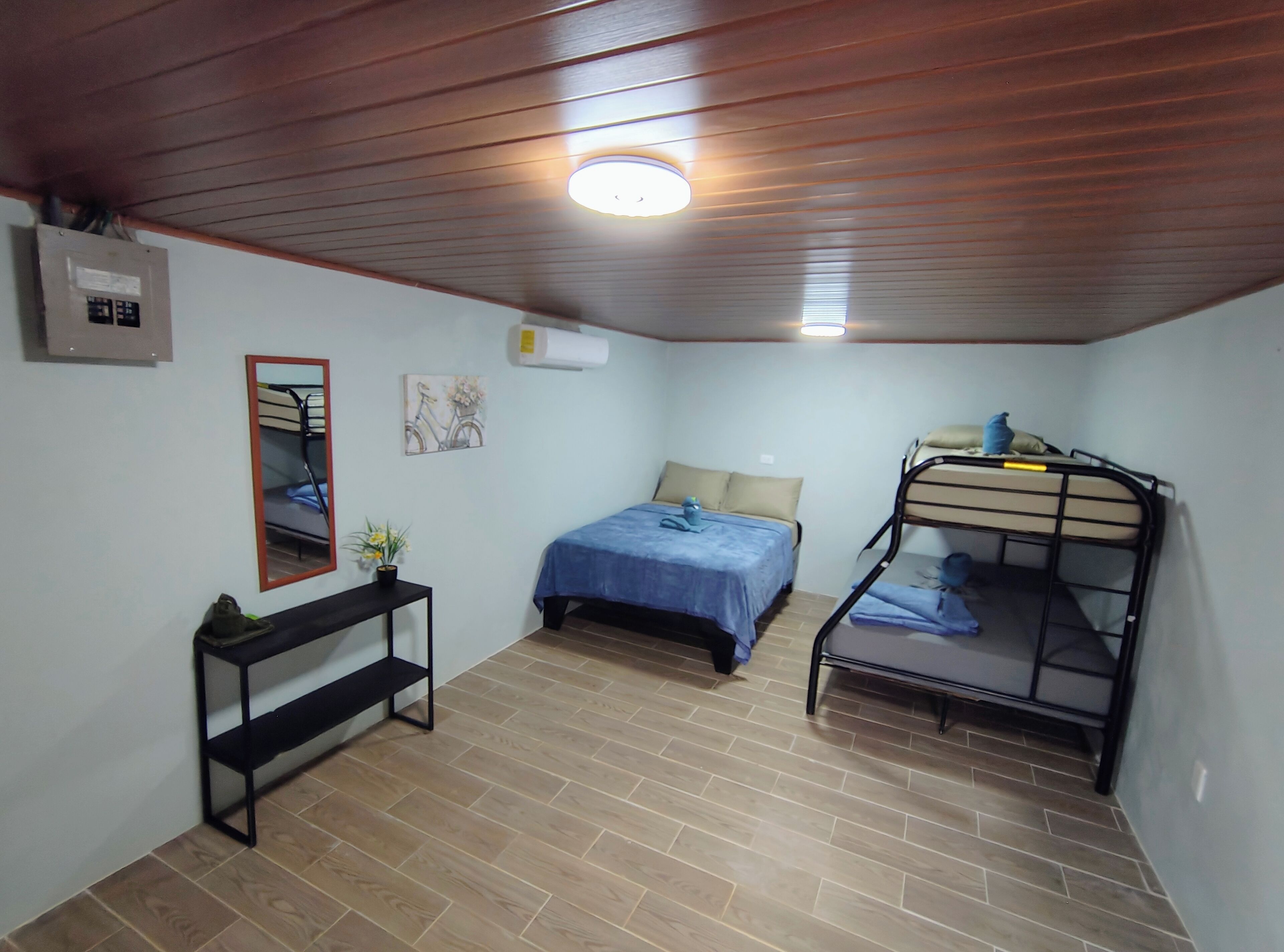 A small, well-lit room with a bunk bed, a single bed, a desk with a chair, and a mirror.
