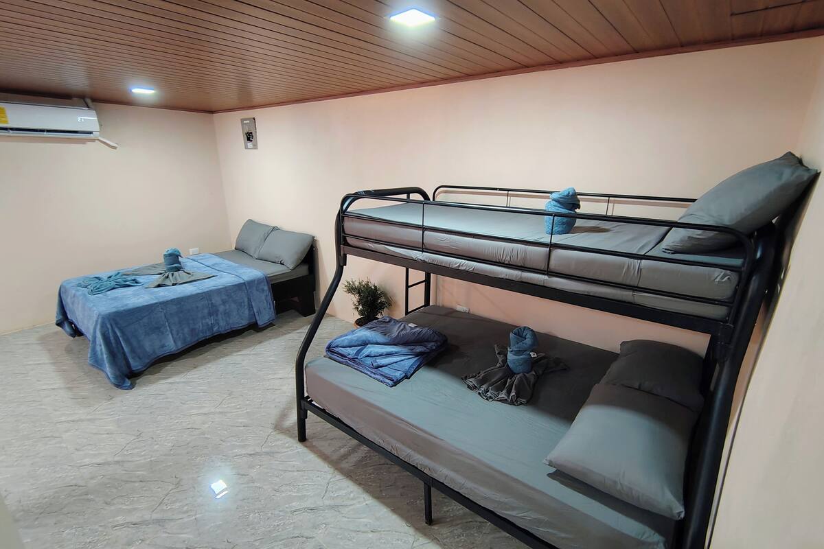 A dormitory room with bunk beds, a single bed, and an air conditioning unit on the wall.