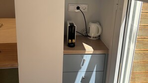Une petite cuisine équipée d’une machine à café, d’une bouilloire électrique Krups et d’une prise de courant.