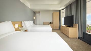 A hotel room with two beds, a TV, a wardrobe, and a view of the city.